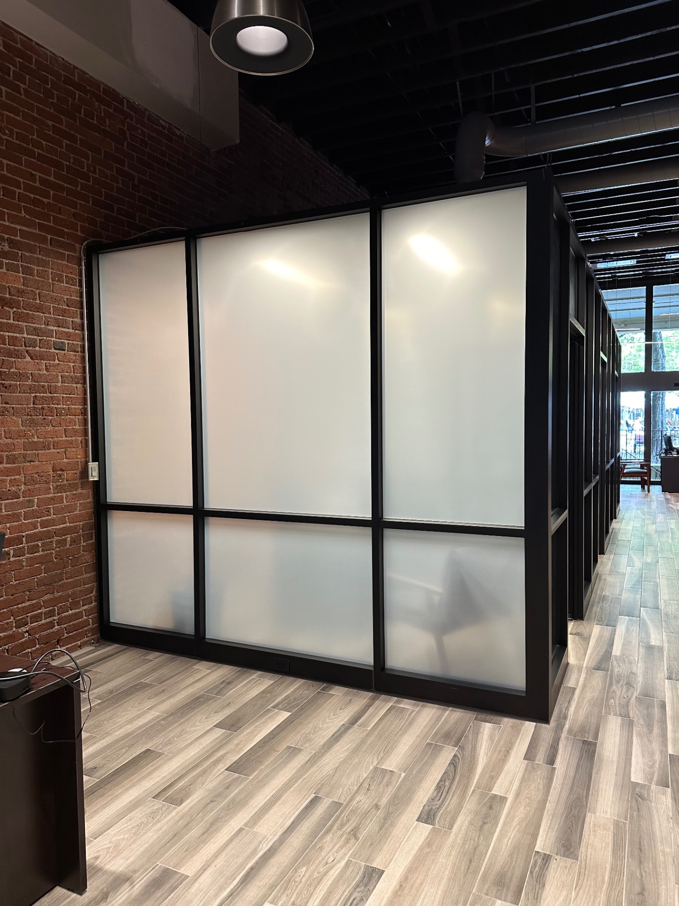 Frosted privacy film on a glass office wall beside exposed brick