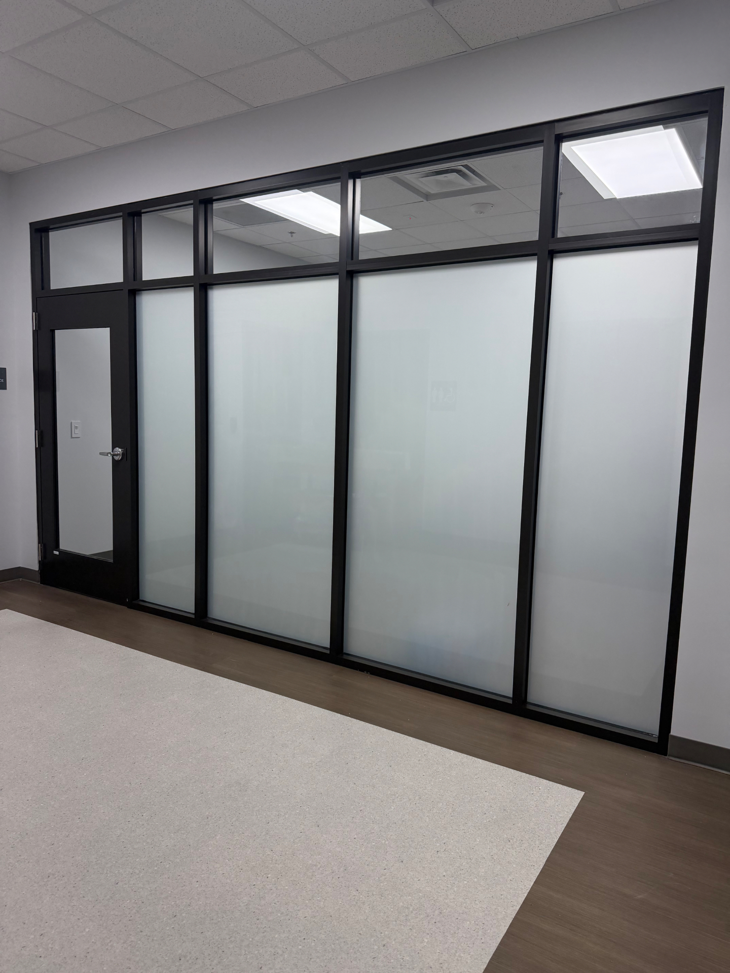 Black-framed glass office partition with frosted film and clear transom